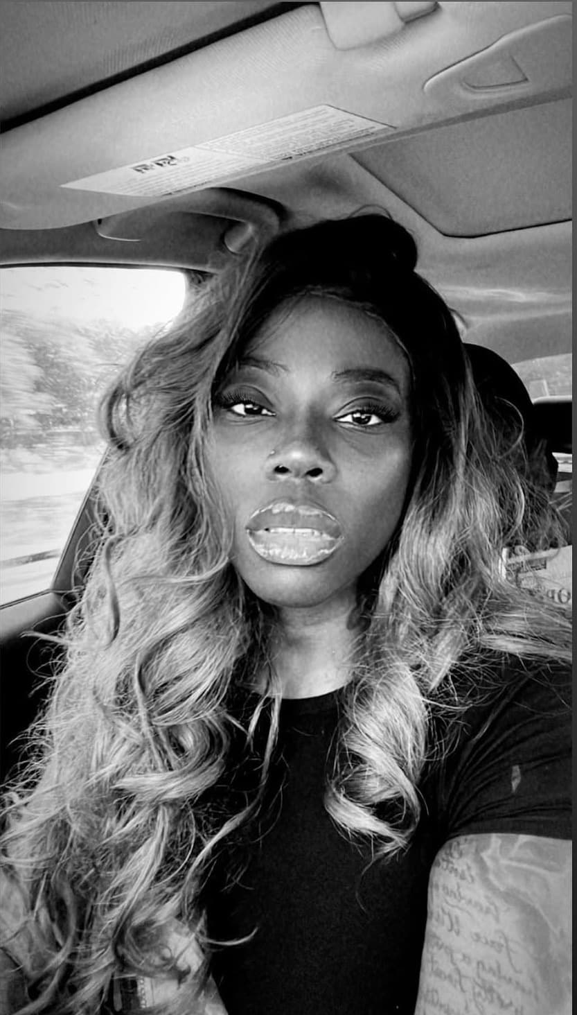 Black and white portrait of a woman with long, voluminous wavy hair inside a car.