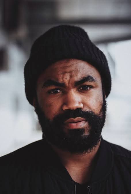 Close-up of a serious Black man with a full beard wearing a black beanie.